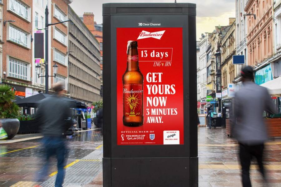 A Budweiser ad on Adshel Live screen on a high street in rainy weather