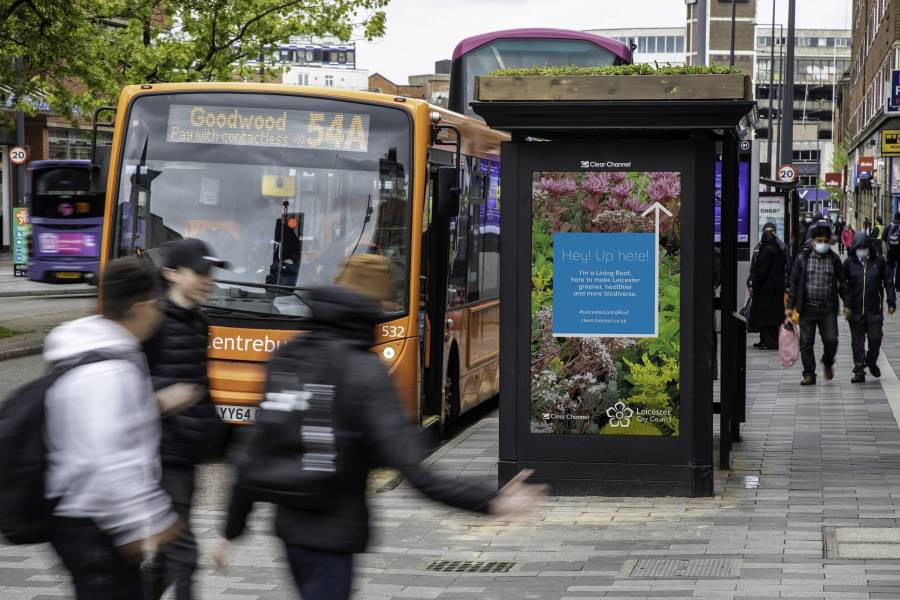 Adshel screen with text saying 'Hey up here!' on a Clear Channel 'Living Roof' bus shelter