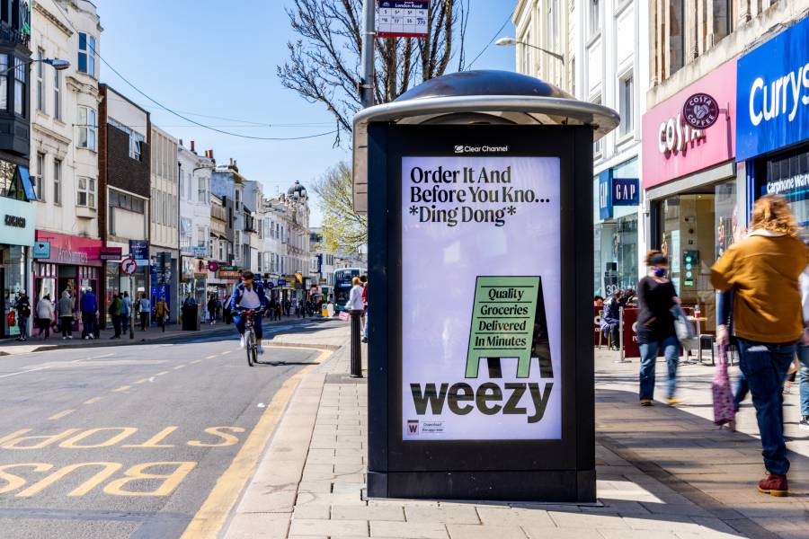 Digital screen on a busy high street showing advert for Weezy app.