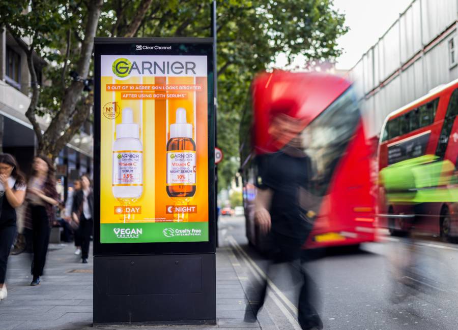 Adshel Live screen in London with two red buses driving past, featuring a bright Garnier advert