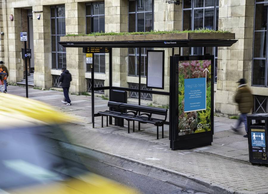 A living roof bus shelter in Leicester with people walking past.