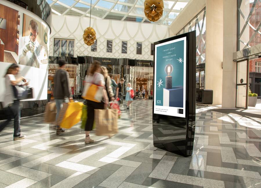 A Malls Live digital screen inside a shopping centre with people waking by