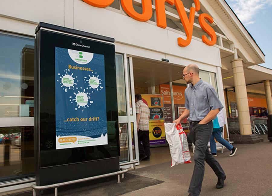 Sainsbury's Live ad outside the entrance of a Sainsbury's as shoppers walk past