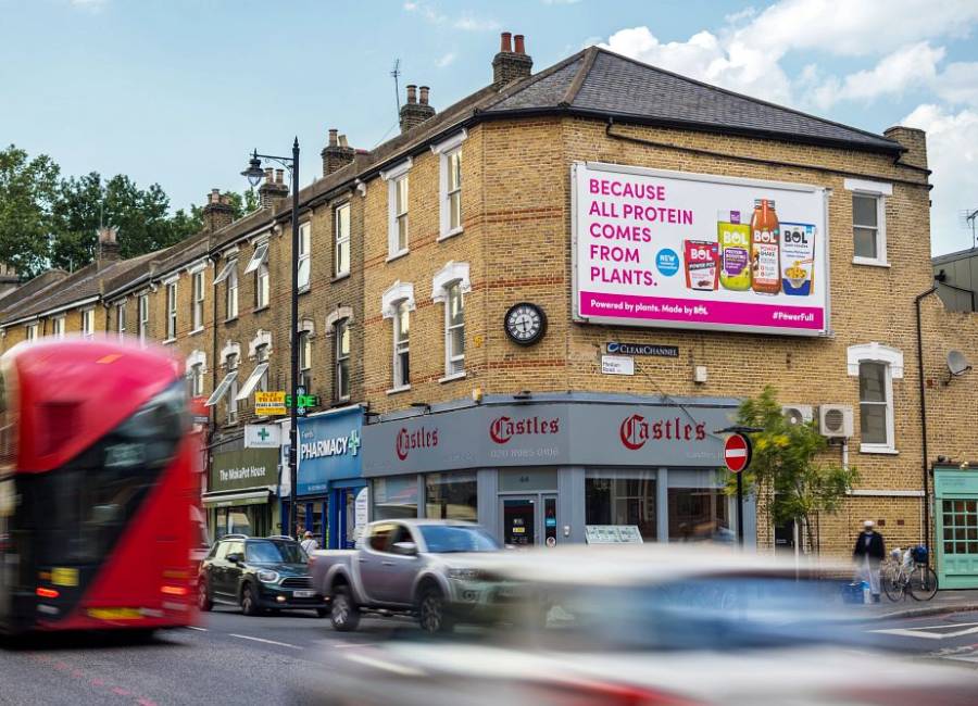 A vegan protein billboard campaign above shops with a bus driving past