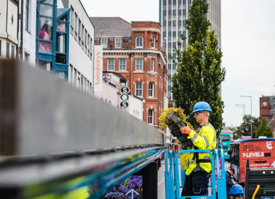 A Clear Channel operative installing a living roof on a bus shelter standing on a cherry picker