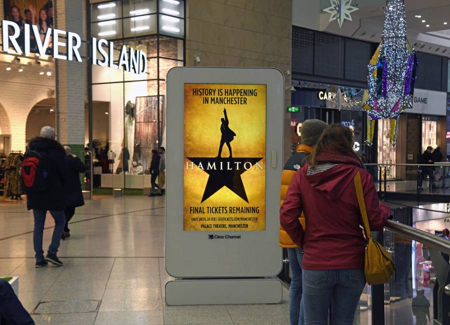 A digital screen inside a shopping mall displaying a Hamilton theatre advert