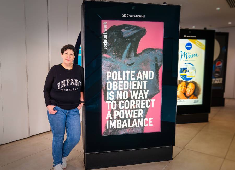 Joanne Harris, novelist, Chair Society of Authors, stands in front of a digital screen displaying her quote and artwork by Martin Firrell, at Clear Channel's HQ in London