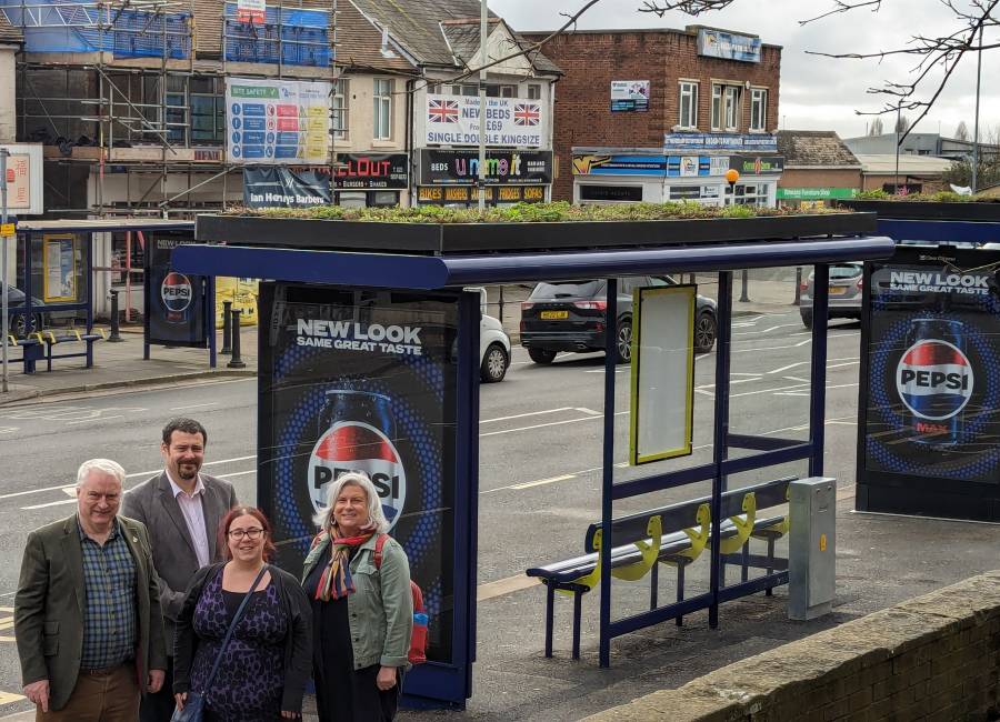 Clear Channel and Portsmouth representatives standing beside a Living Roof bus shelter on a busy street during the day