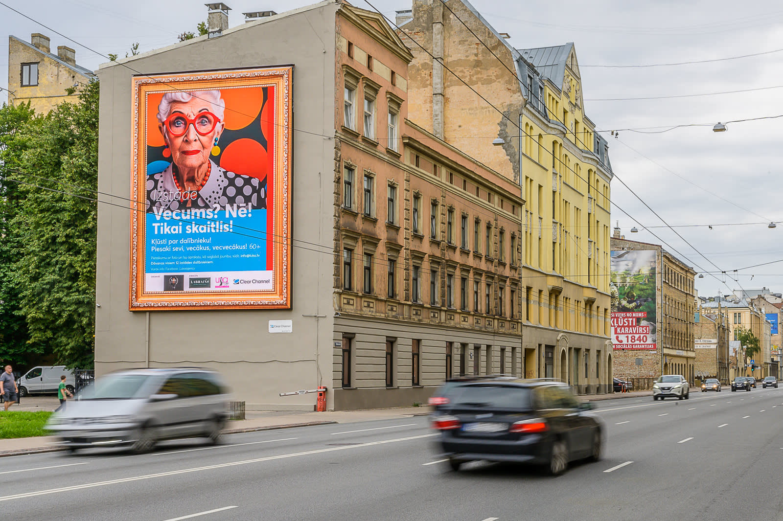 A Clear Channel billboard above a busy road during the middle of the day