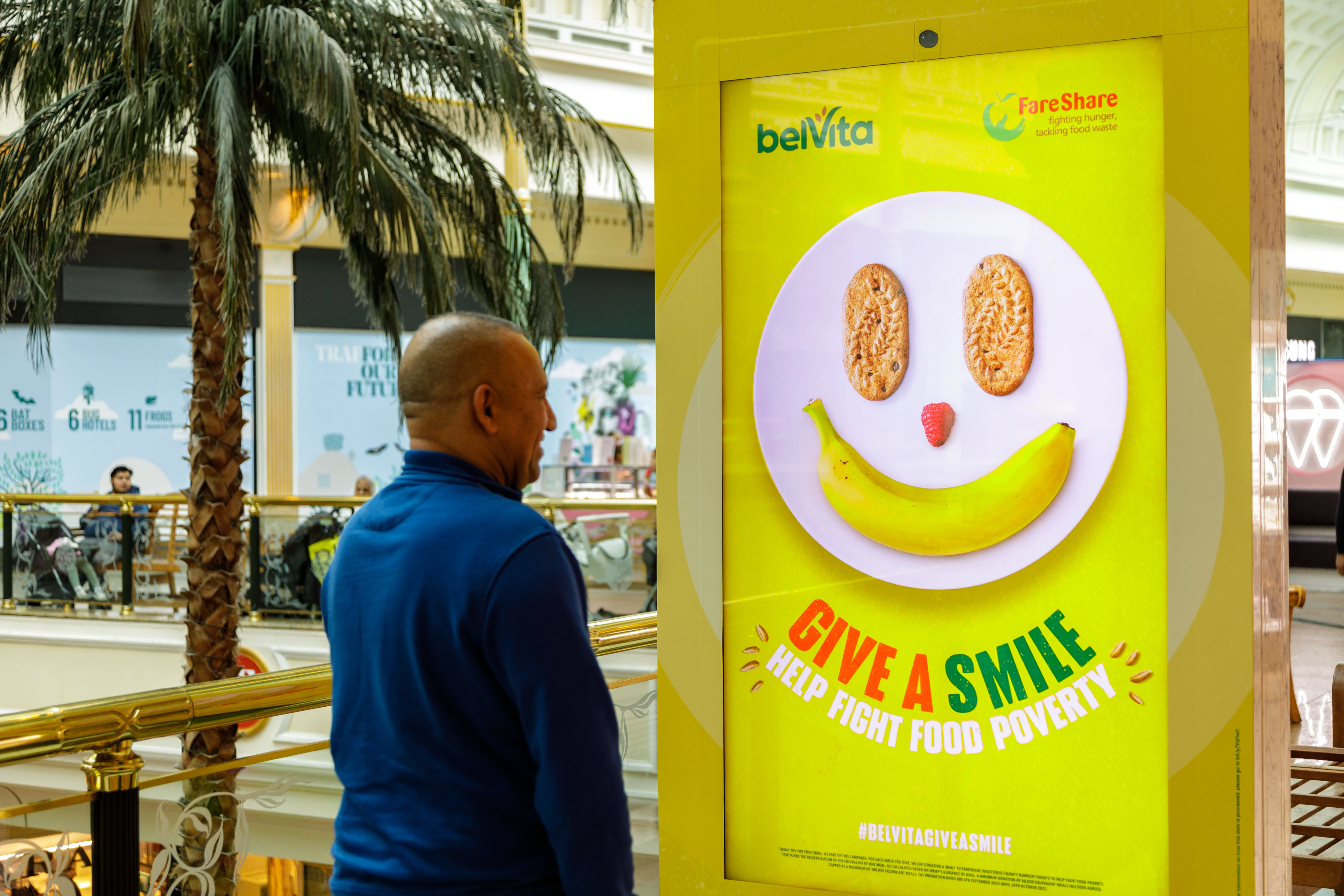 A man smiling and interacting with a Belvita digital screen ad inside a mall