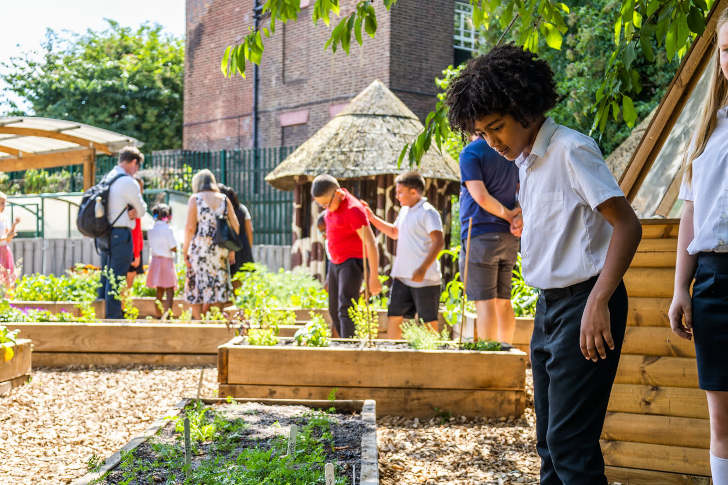 Children in school uniforms looking at wooden boxed planters of crops