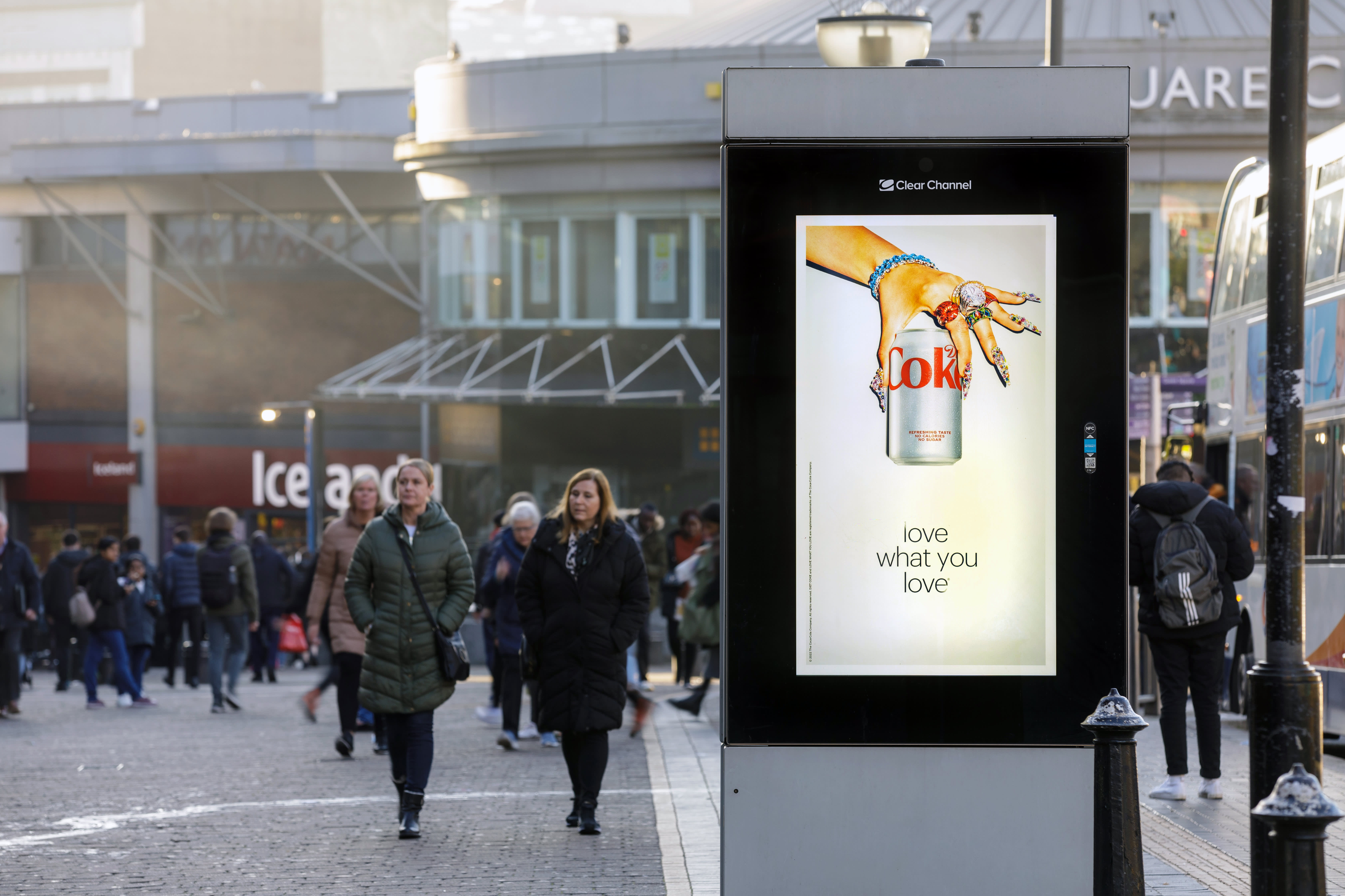 Digital screen on a busy high street showing ad for Coca Cola
