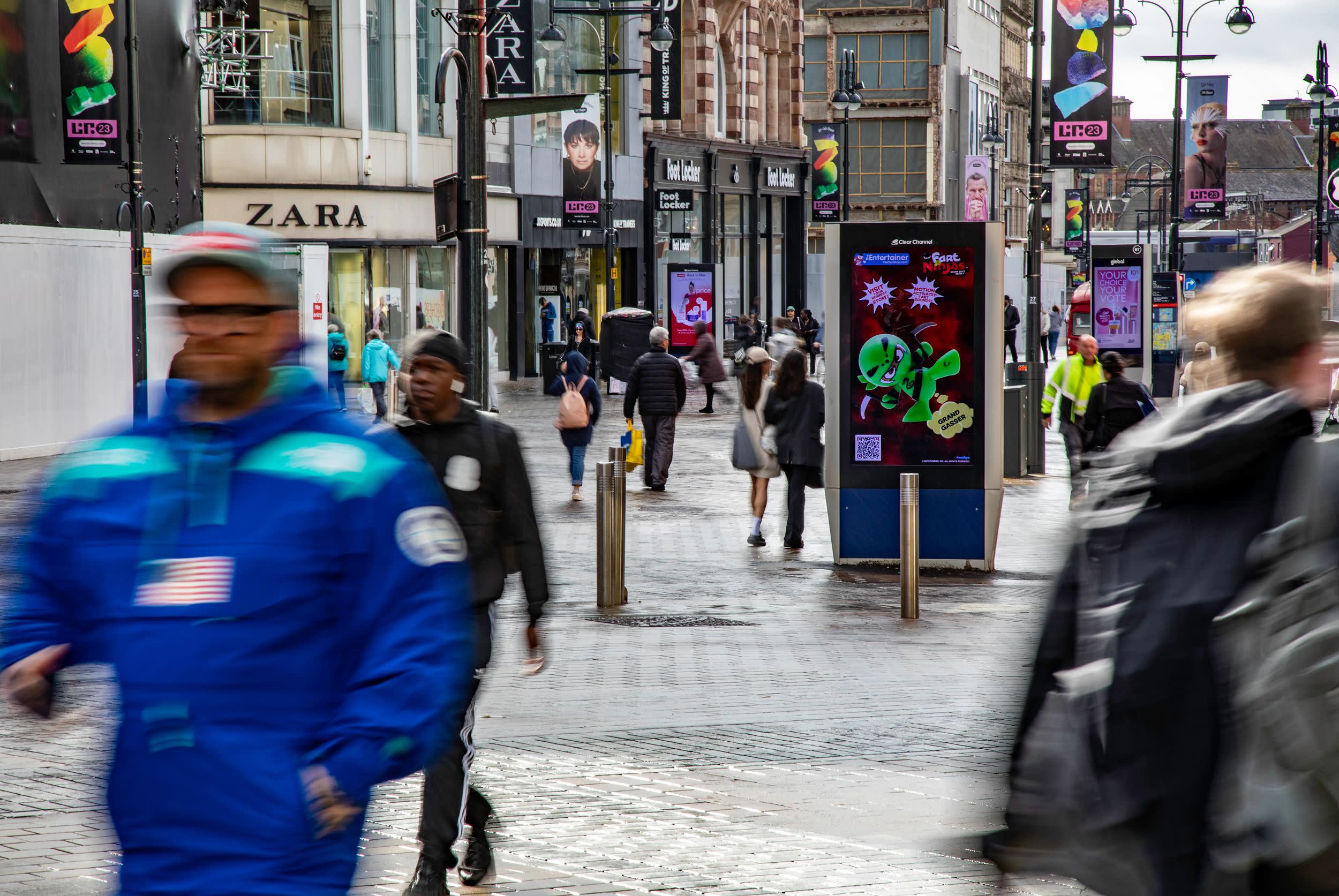 A busy high street with a few Adshel Live digital screens and lots of people