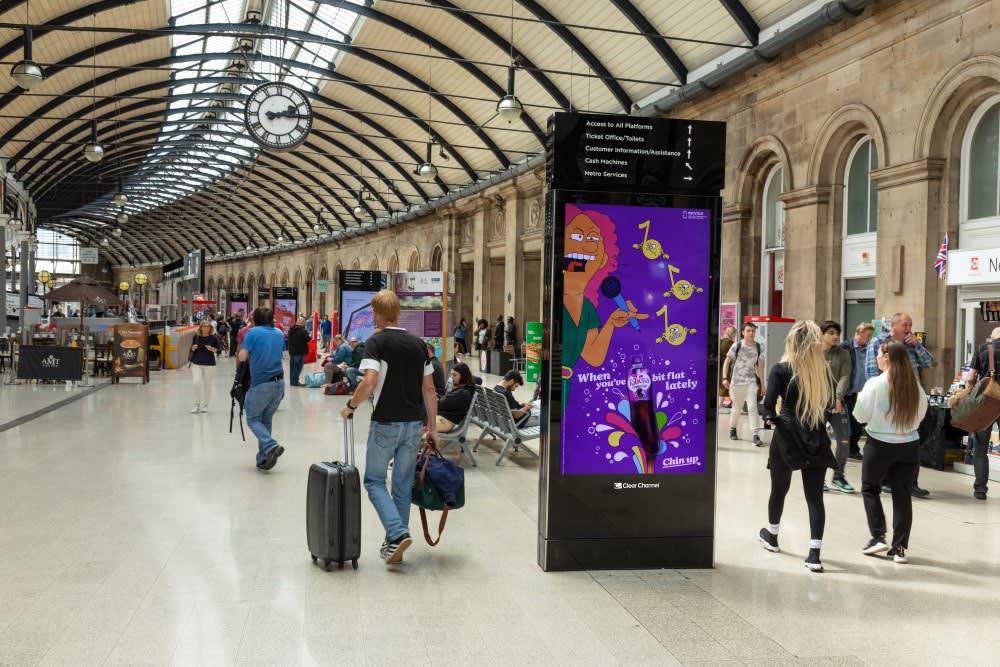 A Station Live digital Out of Home screen inside Newcastle Station with lots of people walking around