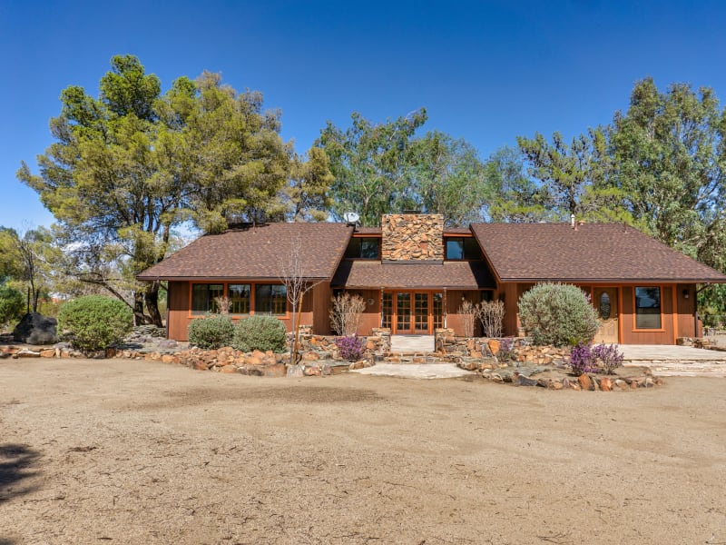 A spacious wooden house with a stone chimney and large windows sits under a clear blue sky.