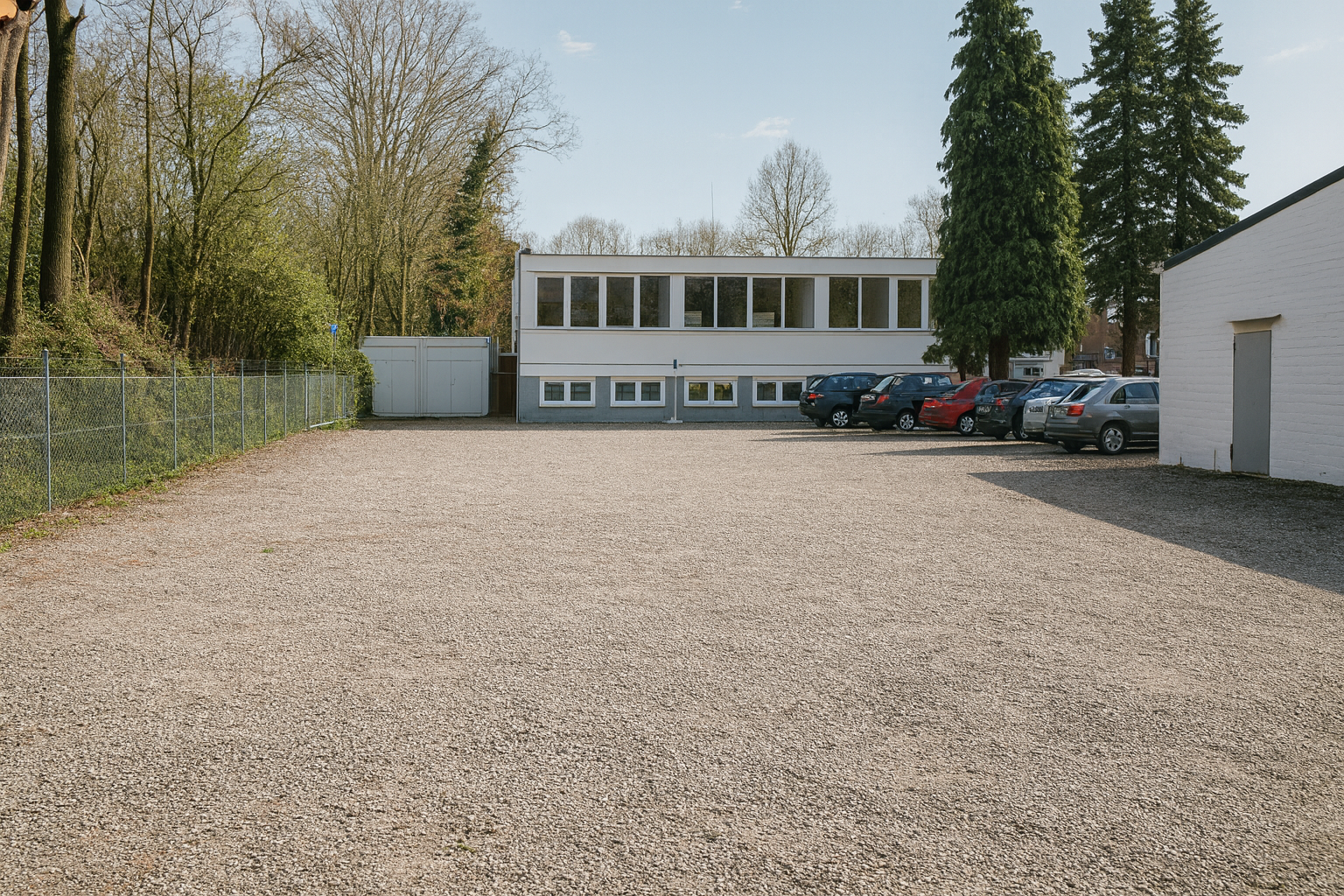 Sonniger Parkplatz von Parkzentrum Hamburg mit sauberem Untergrund, umzäuntem Gelände und modernem Gebäude im Hintergrund