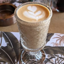 Latte with leaf latte art in a stemmed glass goblet.