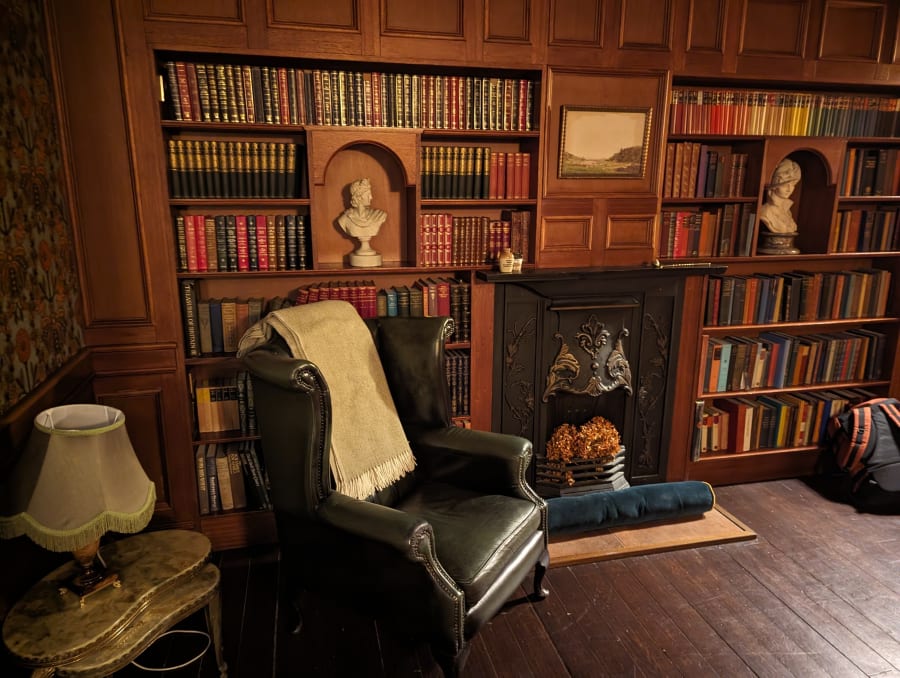 Old-fashioned hotel room with 1920s vibe. Library room with leather armchair, floor to ceiling bookcases, and fireplace.