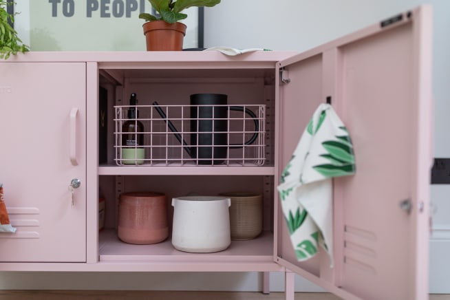 Open locker showing a basket with a mister and watering can on the top shelf, and two pots on the lower shelf