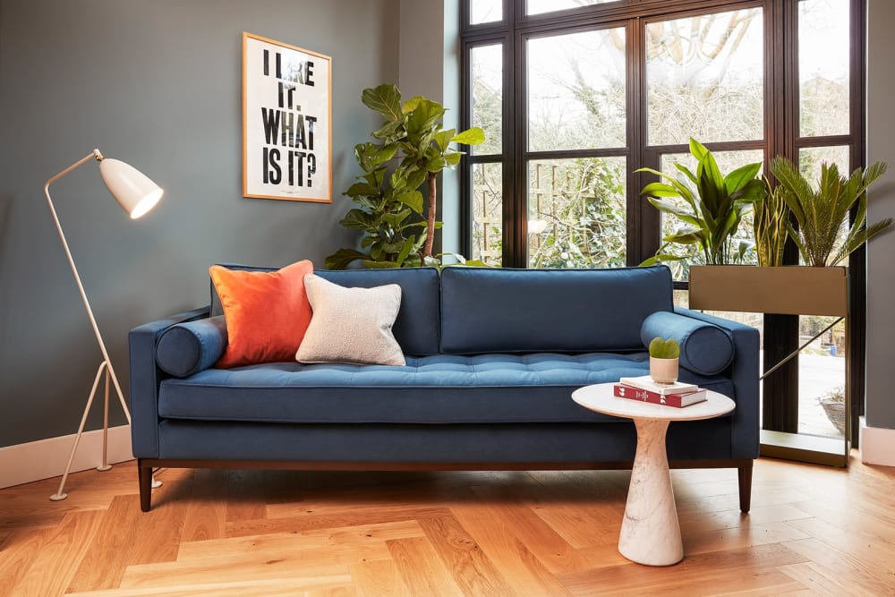 A fiddle leaf fig and a sweetheart plant in a living room with a cycad, snake plant and peace lily grouped together in a tall rectanglur metal plant stand