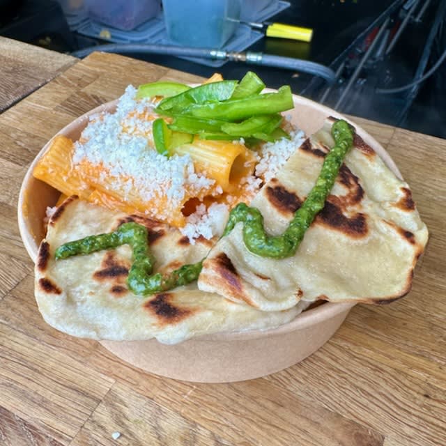 A bowl of pasta with pesto and a fresh made flatbread on the top. Steaming in the cold air