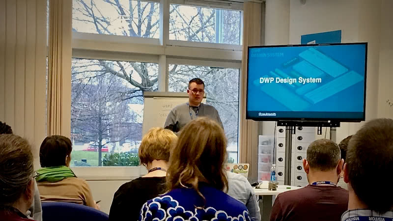 Paul stood in front of a room full of people presenting about the DWP Design System