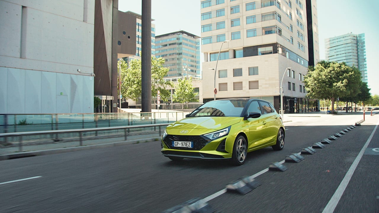 Lime green Hyundai i20 driving through a modern neighbourhood, front view