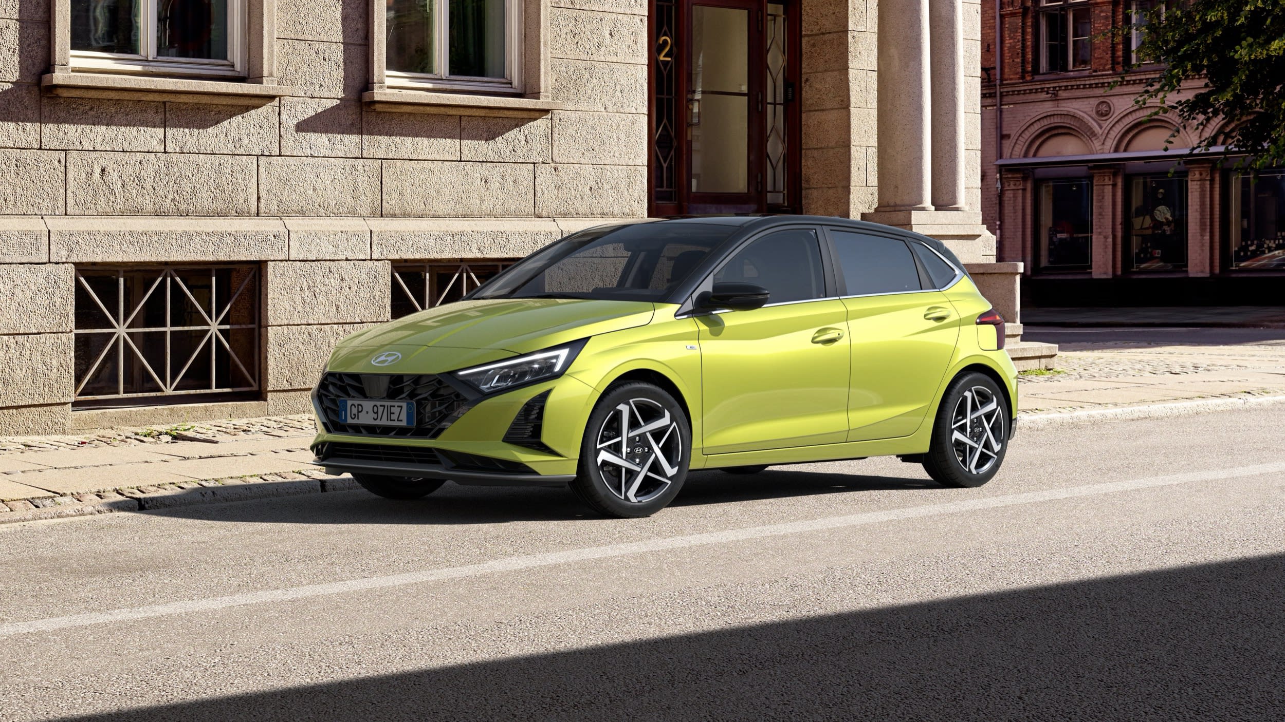 Hyundai i20 verde lima aparcado frente a un edificio de piedra, vista frontal de tres cuartos
