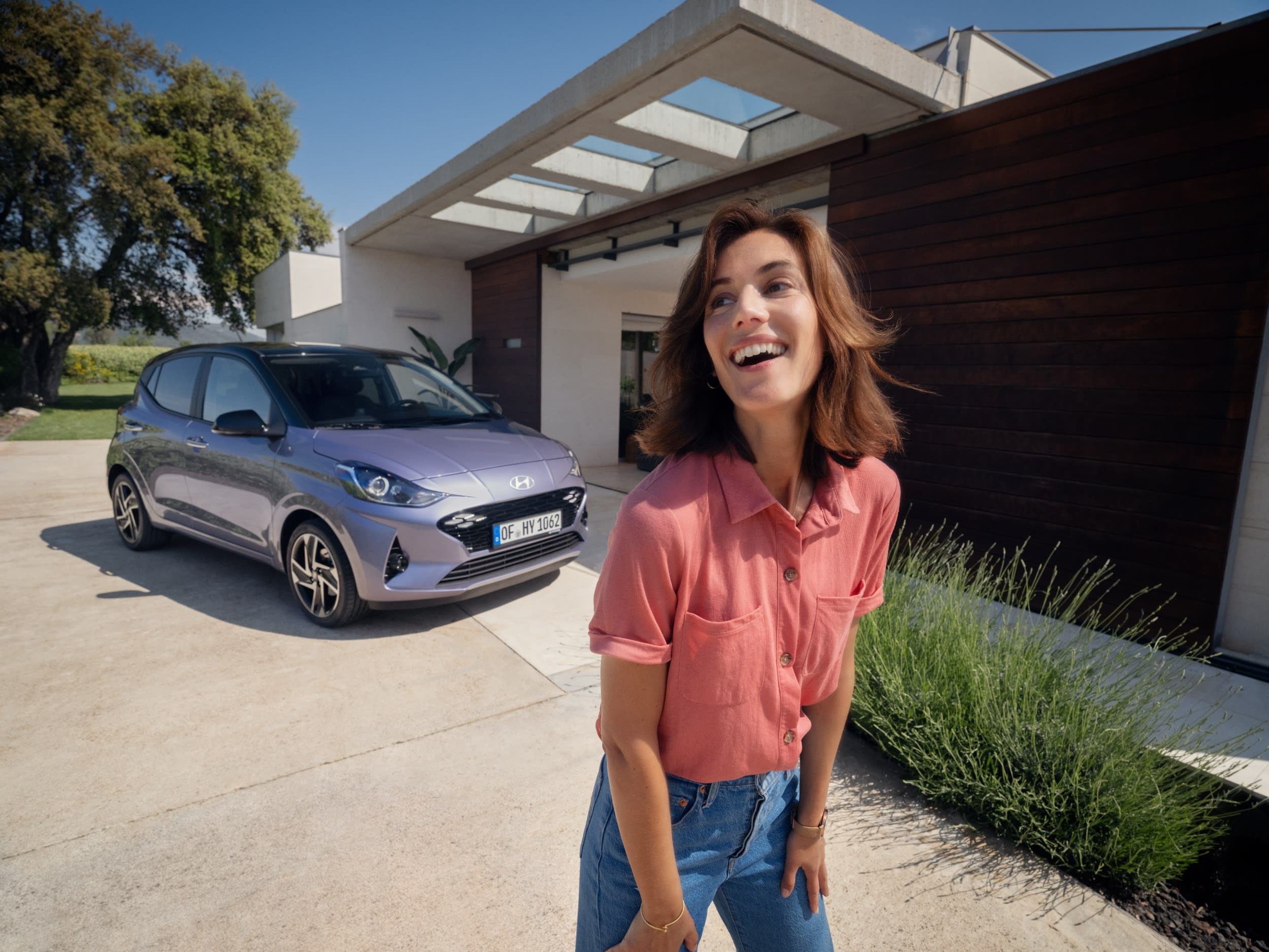 Smiling woman standing in front of a Hyundai i10 outside a modern house