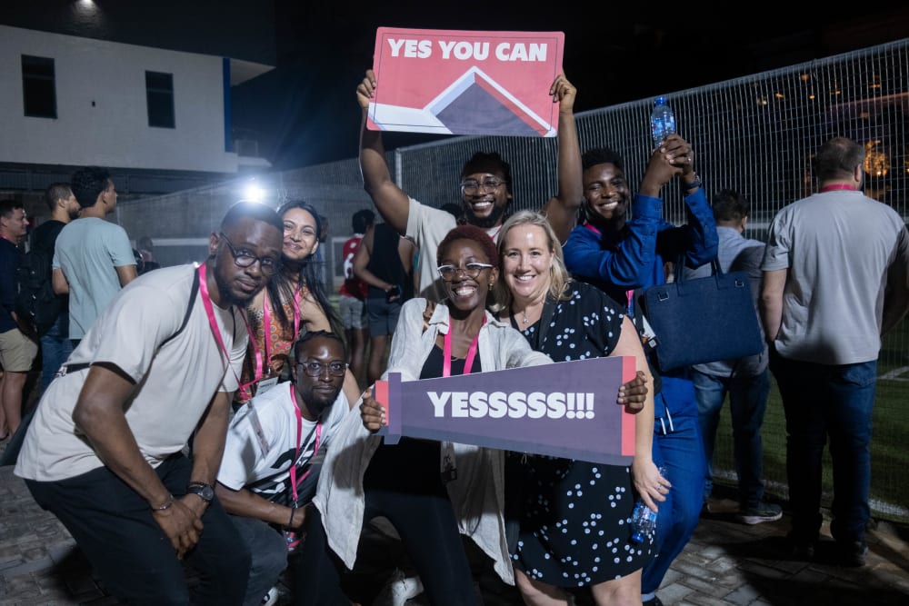 Stacks (Paystack employees) smiling and holding fan signs with the words “Yes you can” and “Yes!” at the 2023 Homecoming Tournament.