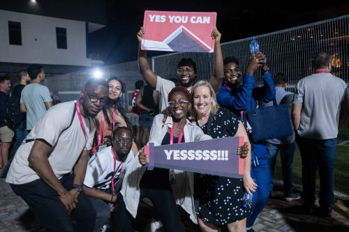 Stacks (Paystack employees) smiling and holding fan signs with the words “Yes you can” and “Yes!” at the 2023 Homecoming Tournament.