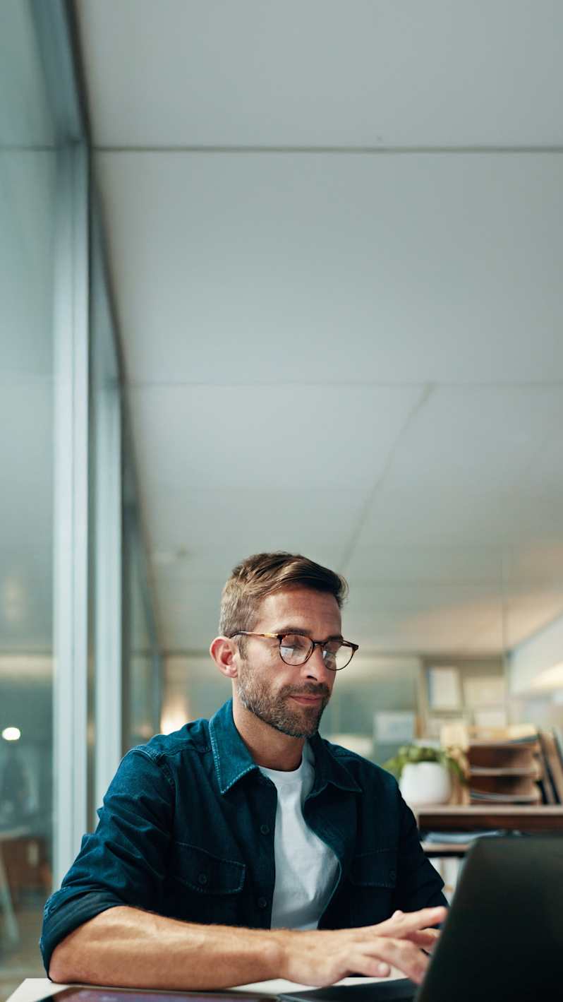 A man with glasses is typing on a laptop.