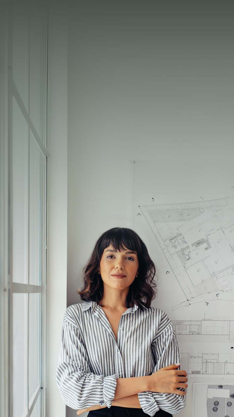 A young architect with her back against a wall in her office.