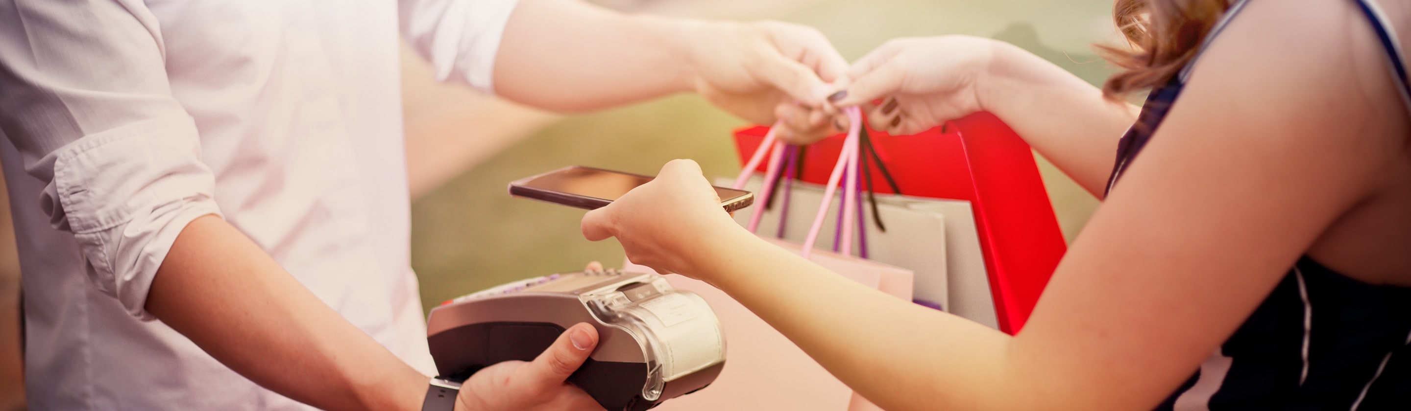 Girl with bags holding her mobile phone to the POS device.