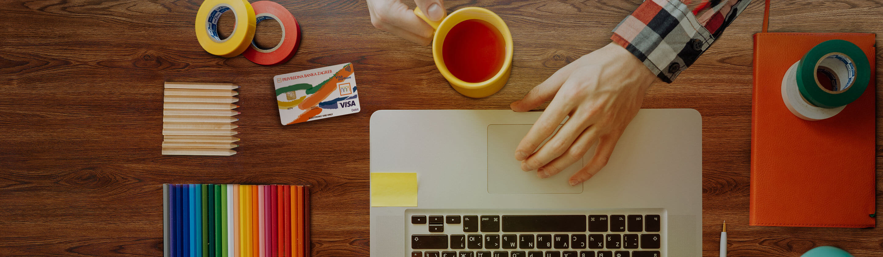 A desk from above with coffee, a laptop, crayons and a Visa Inspire card.