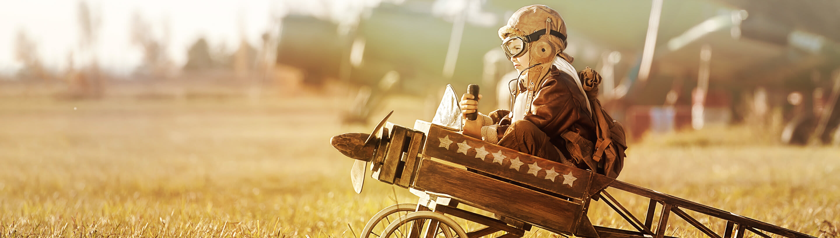 A boy is sitting in a wooden airplane on a runway.