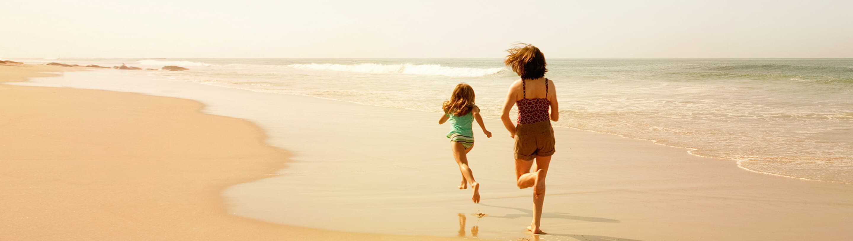 A woman and a girl run along the beach.