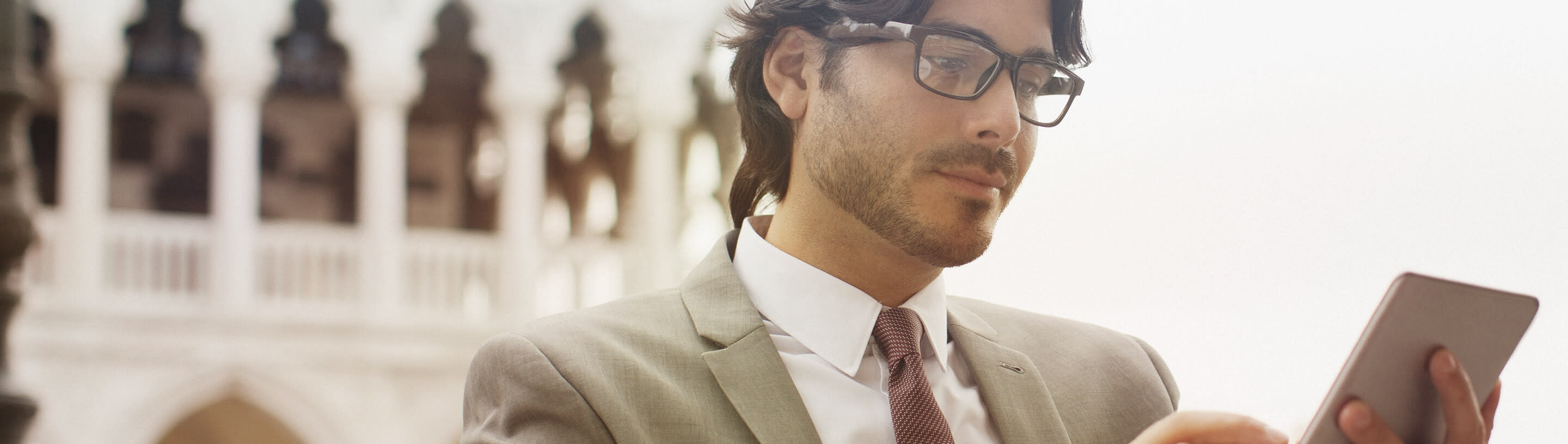 A young businessman sits on a cafe terrace and looks at a tablet.