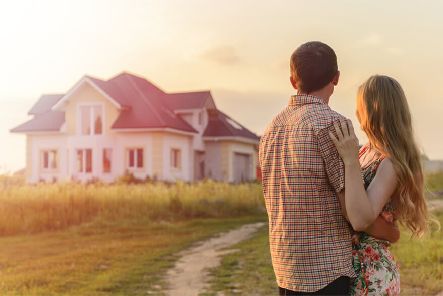 A young man and a girl in an embrace look at a house in the distance.