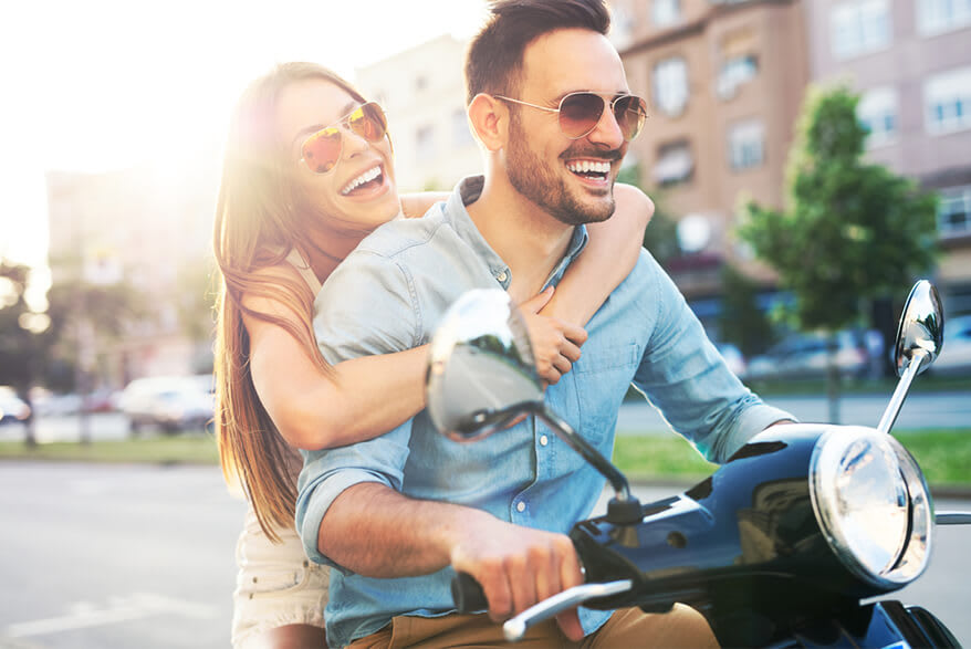 A smiling young man and a girl riding a motorbike.