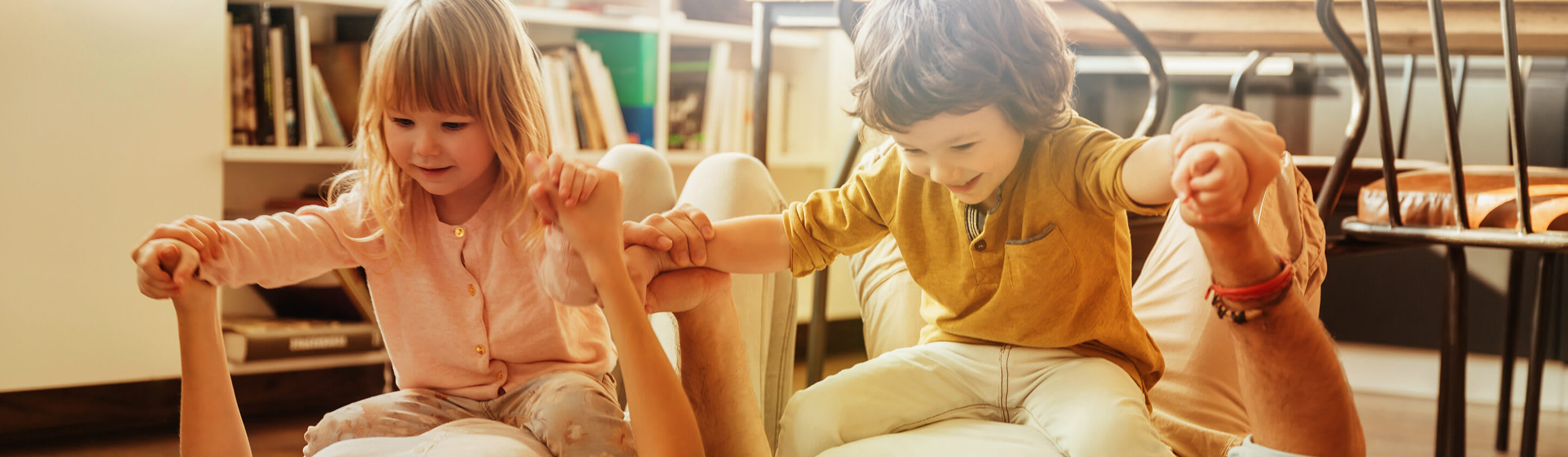 A girl and a boy are sitting on their parents who are lying on the floor.