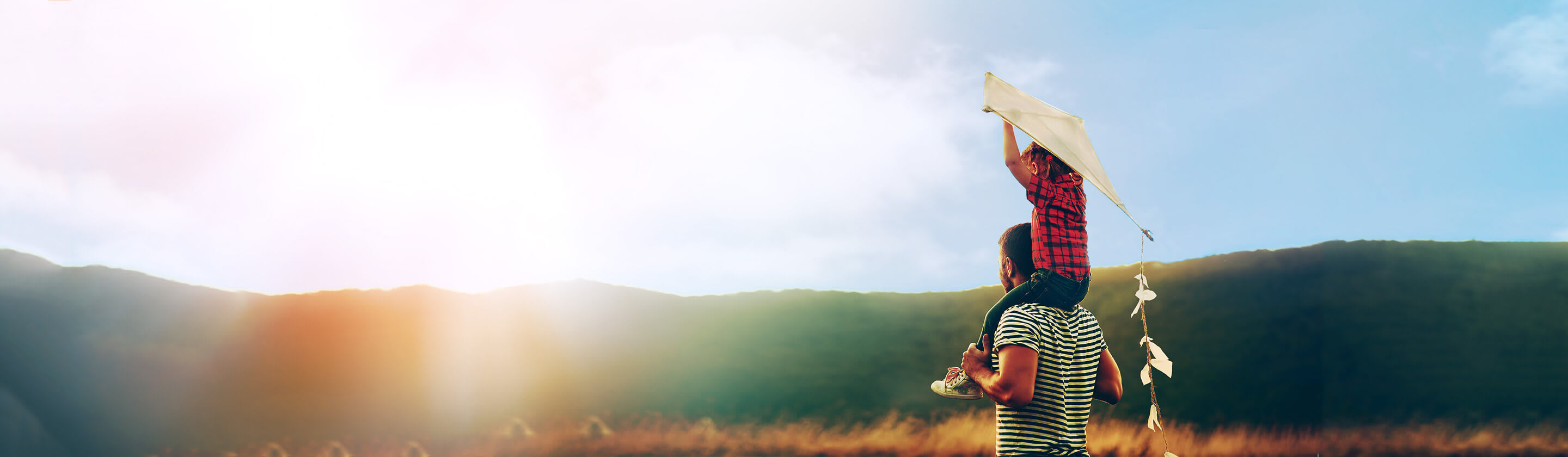 A boy with a kite sits on his father's shoulders.