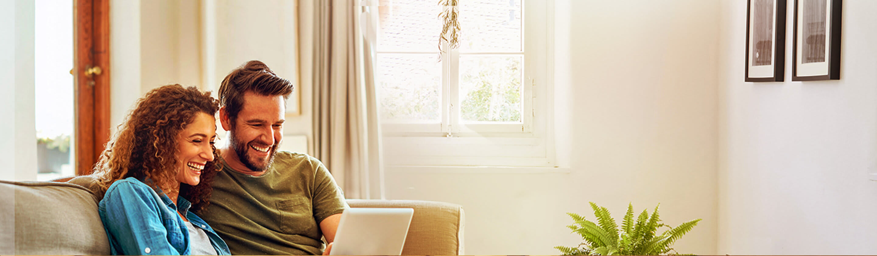 A smiling couple sits on a couch and looks at a laptop.