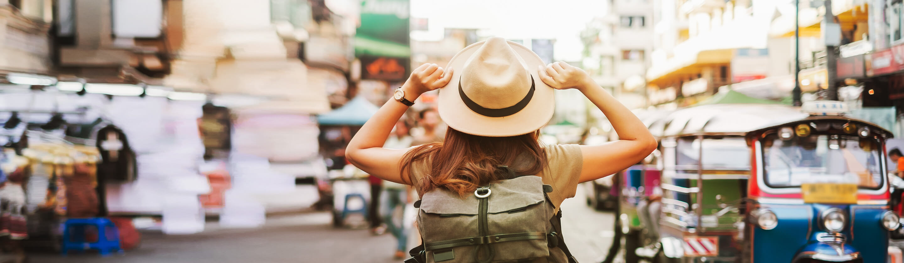 A young tourist with a hat and a backpack on her back walks down the street.