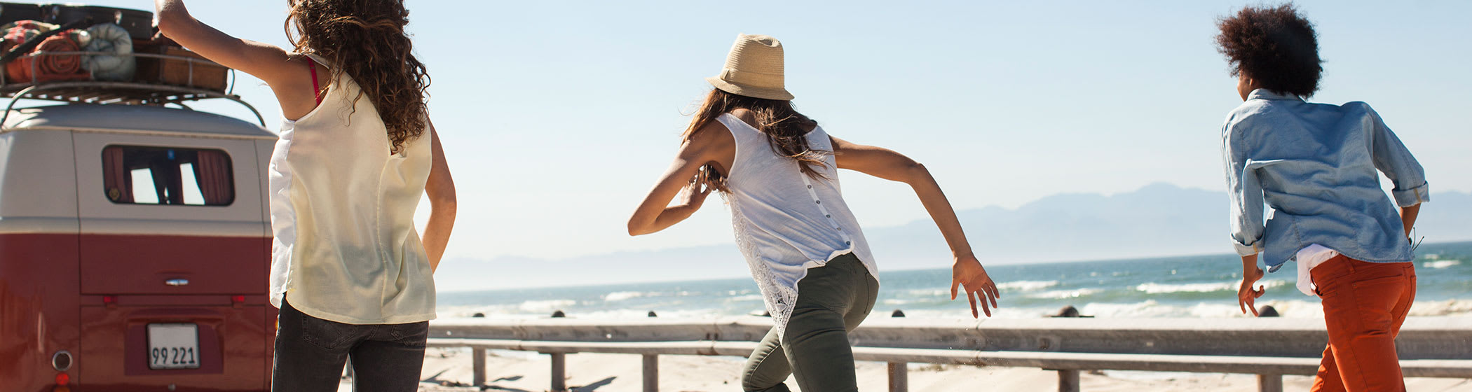 Three young girls with their backs turned running towards the beach