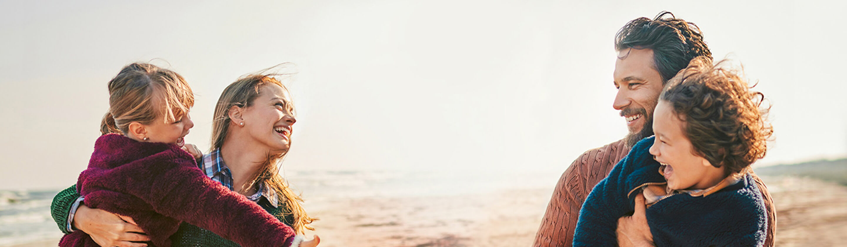 A father and mother with two children stand smiling by the beach.