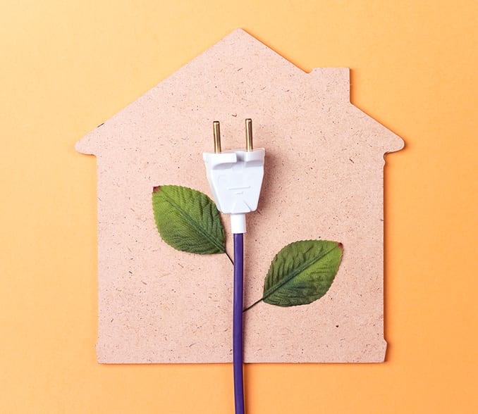 A house shape cut out of cardboard on an orange background with an electrical cable.