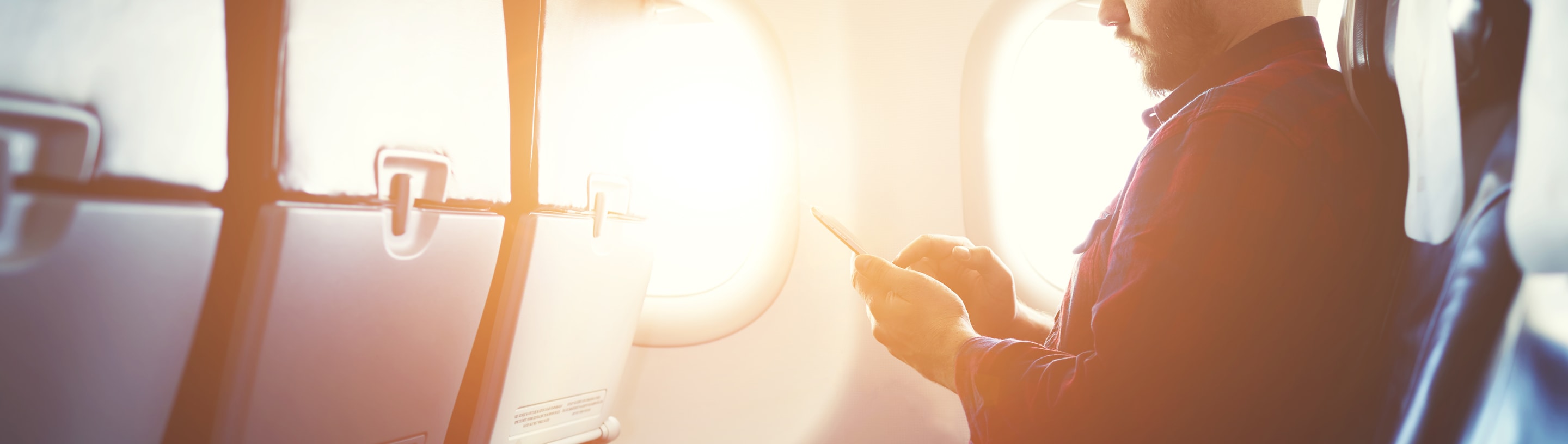 A man sits on a plane looking at his cell phone.