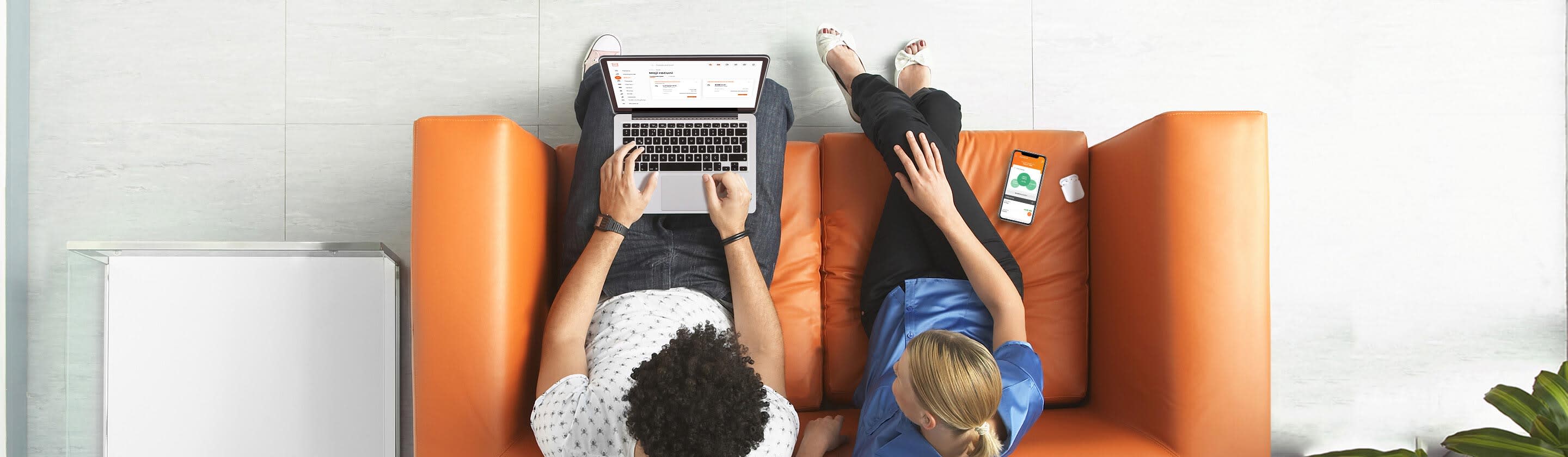 A young couple is sitting on an orange couch and looking at a laptop.