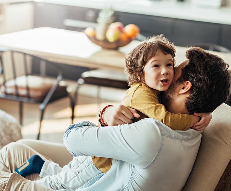 A father and a little son sit on a chair, hugging each other.